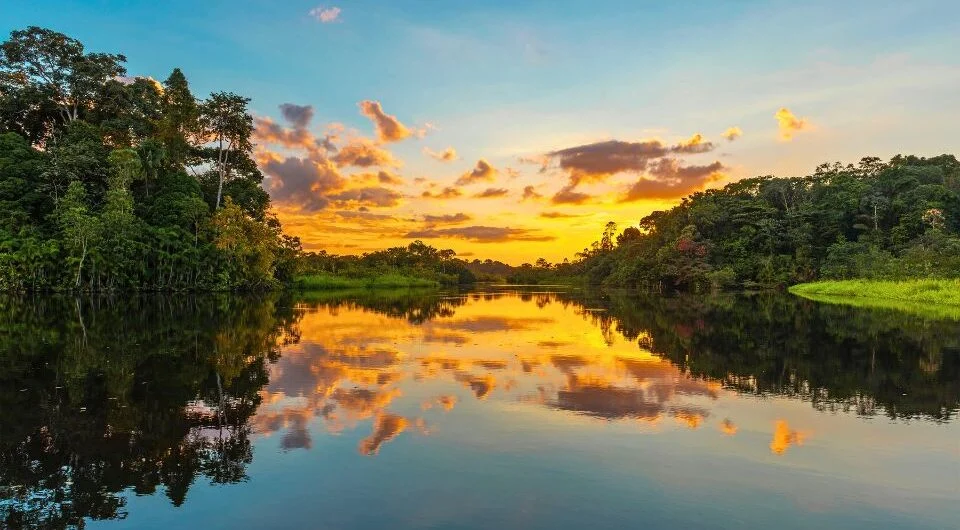 Rio entre a floresta amazônica, com o pôr do sol refletido na água.